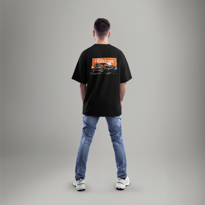 Black oversized t-shirt featuring a vintage Ford Mustang graphic on the back with an orange grunge background – worn by a male model facing away.